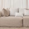 Coussins en lin HECTOR 40x60cm, HORACE 50x50cm, HYPOLITE 25x40cm, coloris WHITE, thème HANDMADE, avec coussin en lin 50x50cm CROSS, coloris Snowy, thème FARM LIFE, sur canapé en lin coloris Naturel, ligne SLOW, module d'angle COIN et chauffeuse SOLO