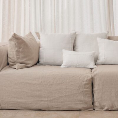 Coussins en lin HECTOR 40x60cm, HORACE 50x50cm, HYPOLITE 25x40cm, coloris WHITE, thème HANDMADE, avec coussin en lin 50x50cm CROSS, coloris Snowy, thème FARM LIFE, sur canapé en lin coloris Naturel, ligne SLOW, module d'angle COIN et chauffeuse SOLO